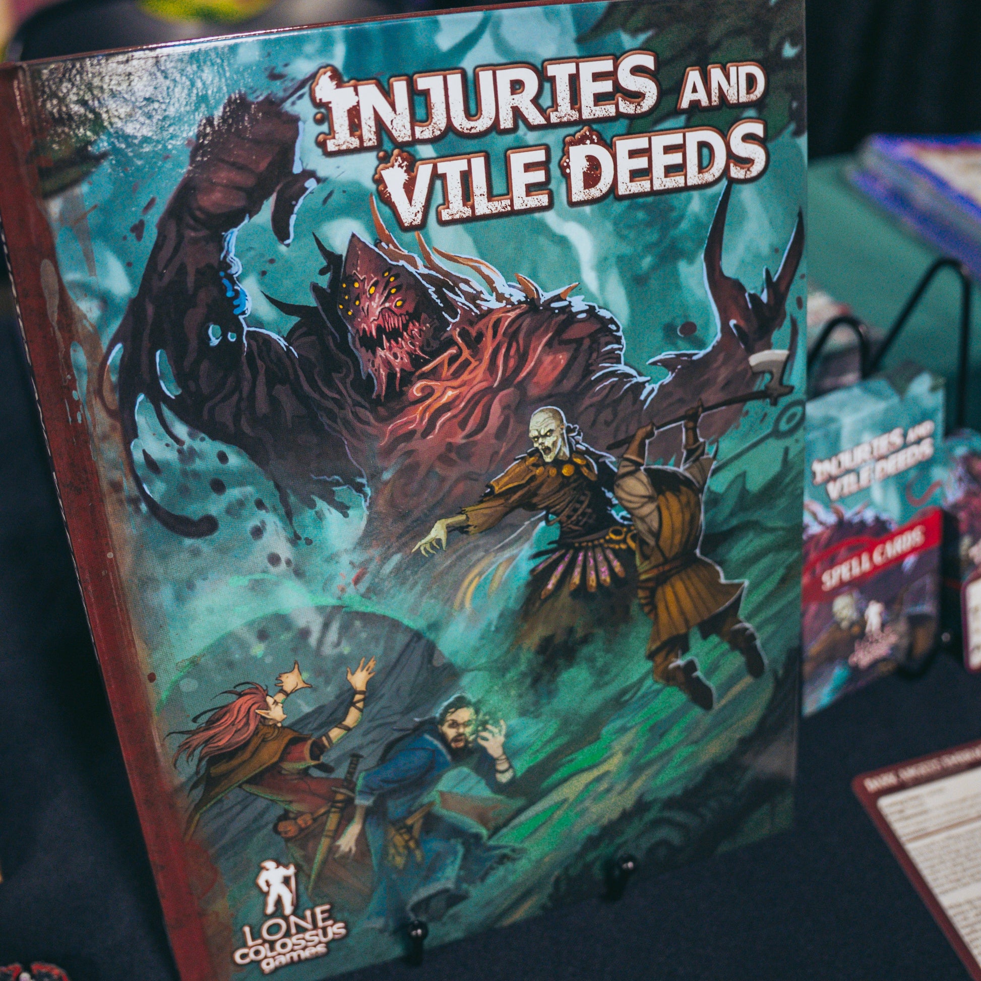 Photo of the hardcover of Injuries and Vile Deeds, a dark fantasy supplement for D&D 5e encouraging tactical, cinematic combat with injury systems, monsters, NPCs, subclasses, spells, magic items, backgrounds, feats, and more